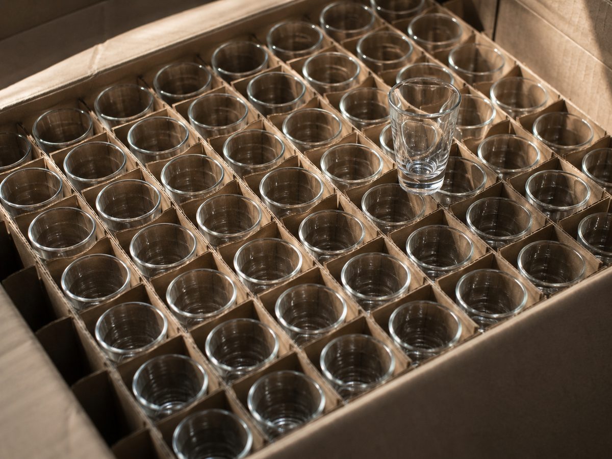 Dozens of clear shot glasses packed in a partitioned kraft carton, rims catching window light